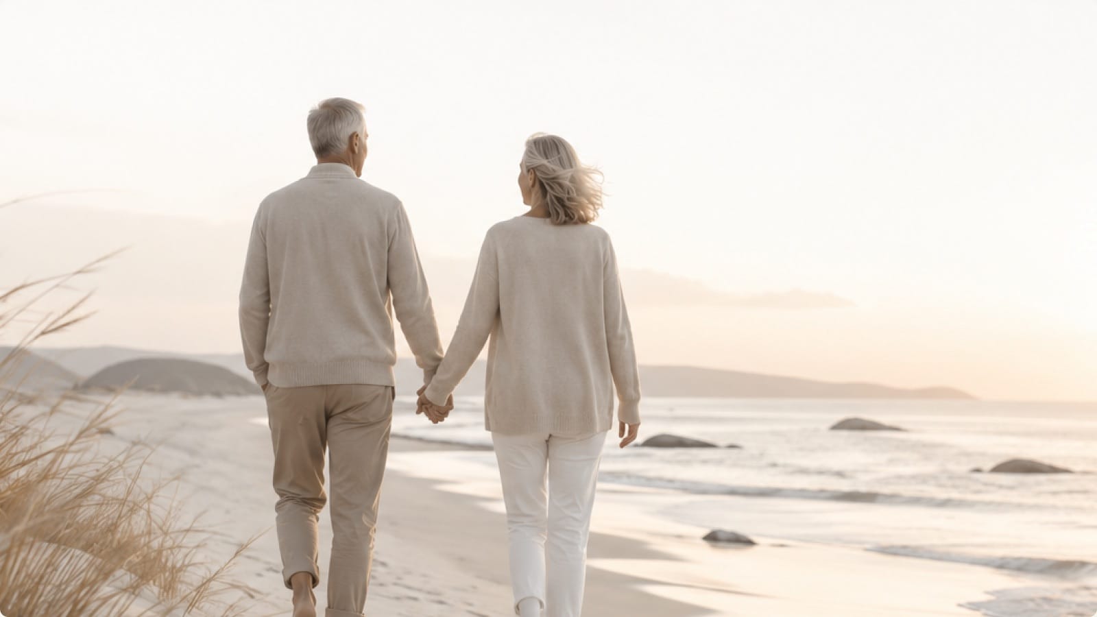 An older couple walking hand in hand along a coastal path at sunset.
